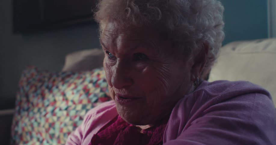 An elderly woman is smiling joyfully indoors lit warmly in a cozy setting