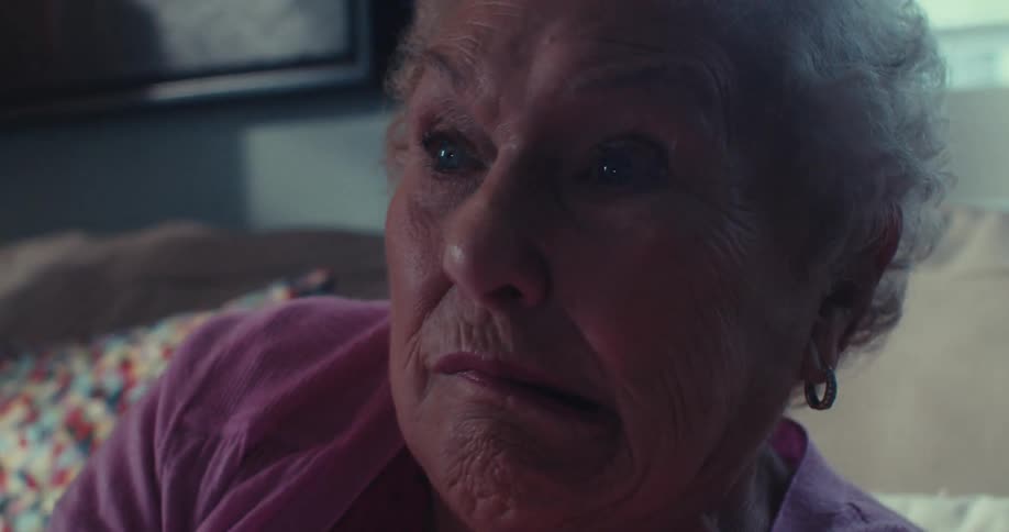 Elderly woman makes anxious and happy faces while playing video games with a controller in the living room