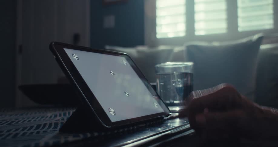 An elderly person interacts with a tablet using their finger in a dimly lit home setting