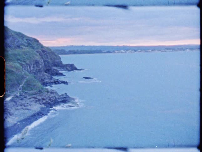 A scenic aerial view captures rocky cliffs meeting the calm ocean under a dusk sky