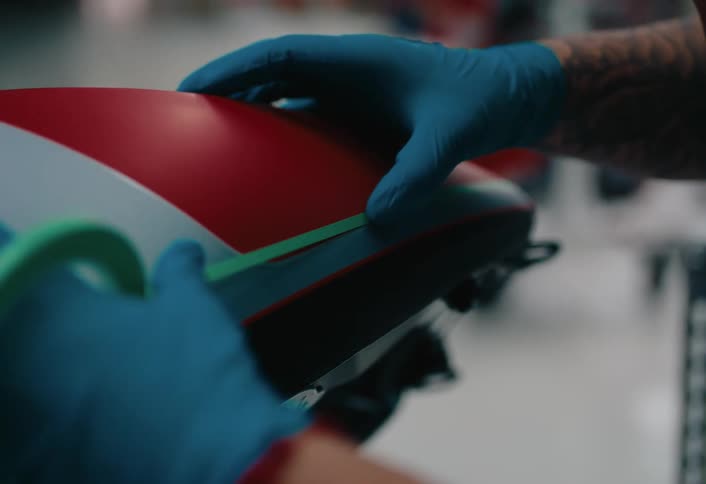 A worker applies a stripe line design to a motorcycle in a workshop