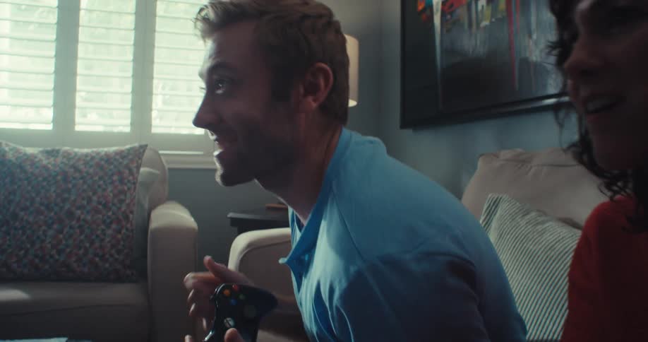A couple sits on a couch playing video games holding controllers and celebrating with excitement and joy