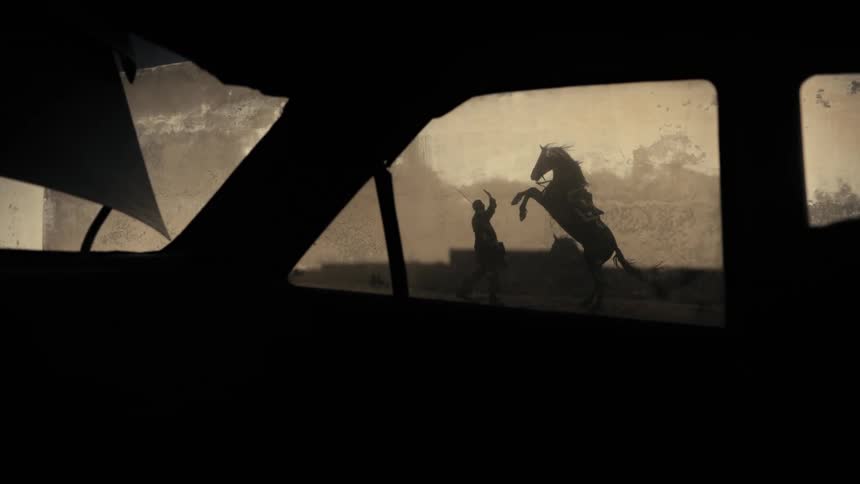 Through the car window a horse can be seen jumping in front of a man