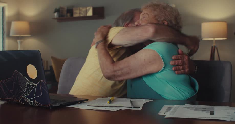 A man and woman hug in front of their laptop
