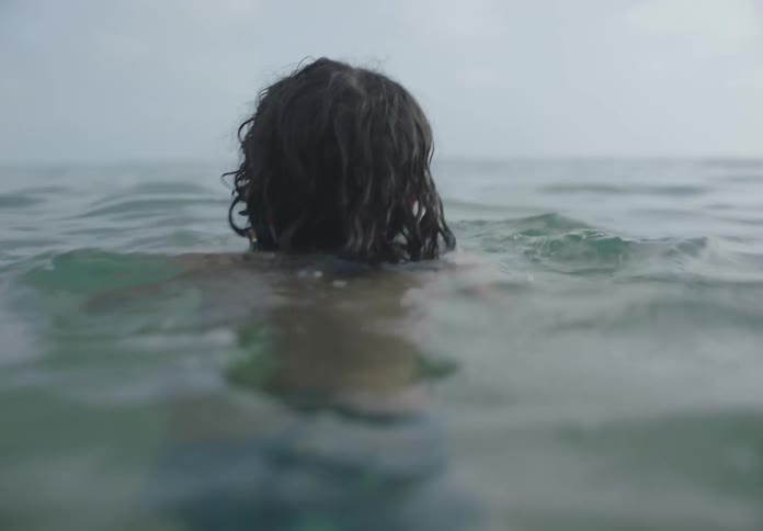 A child with long hair swims in the ocean at midday
