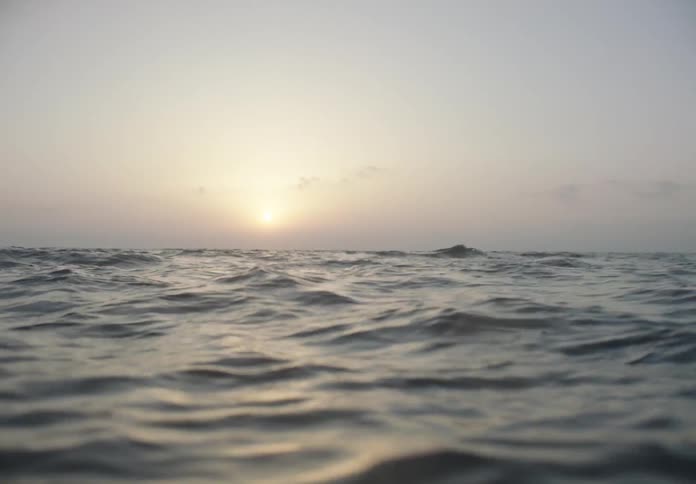 The sun is rising in the cloudy sky over the ocean