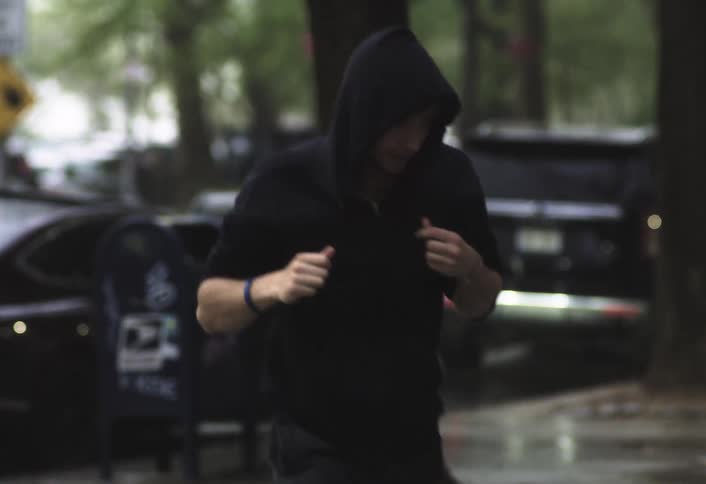 Man wearing a hoodie runs on the wet sidewalk near a city street