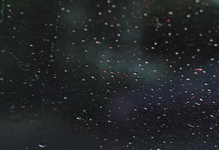 Rain falls on a car windshield as the wipers clear the water off the glass at night in the middle of the road
