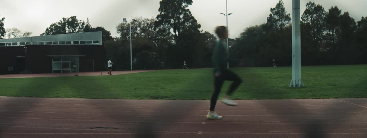 A woman is running on a track field under a cloudy sky