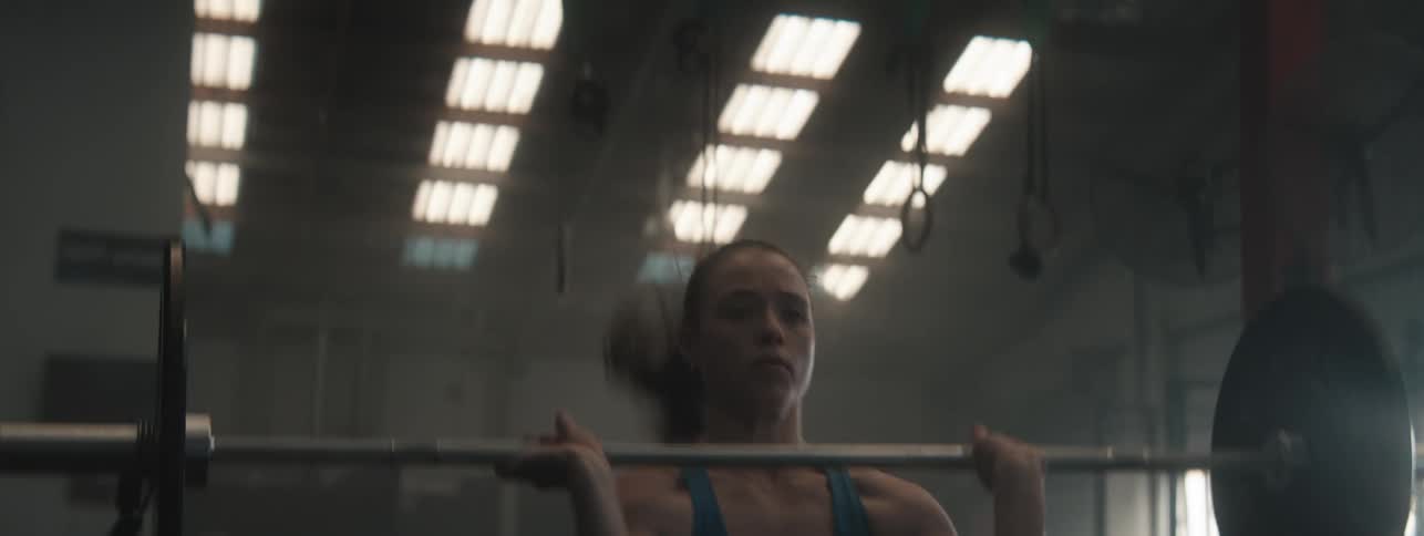 Young woman lifts a weight bar while exercising in an empty gym during the daytime
