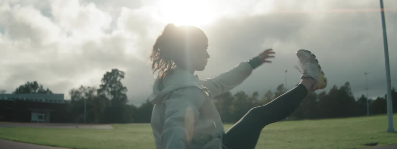 The woman is kicking her legs on the track to stretch