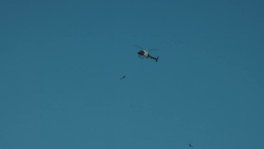 A black and white helicopter flies around near other helicopters below a clear blue sky