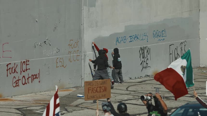 Some protesters hold flags or signs while others paint graffiti messages protesting the ice agency