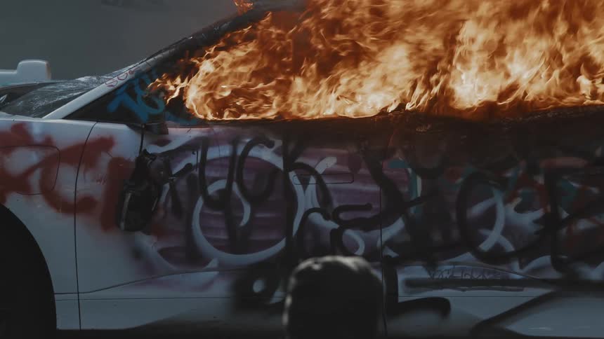 A car with graffiti on it is burning up in flames