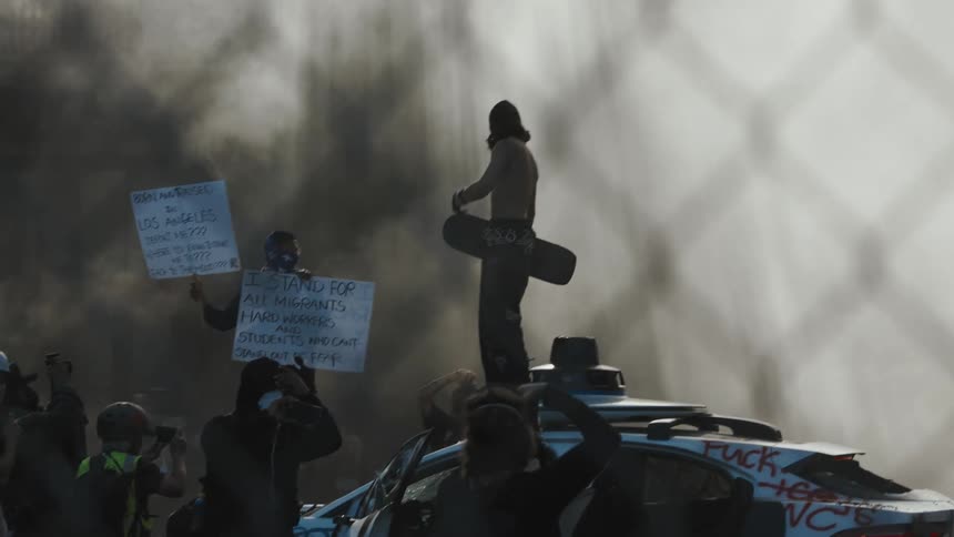 A man is standing on a car during a riot