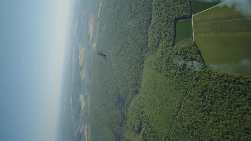 Aerial view of a plane releasing smoke flying over a natural area