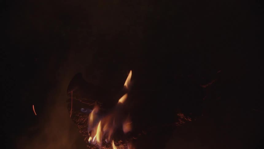 Roaring fire burns the head of a pig releasing a cloud of smoke while it cooks at night