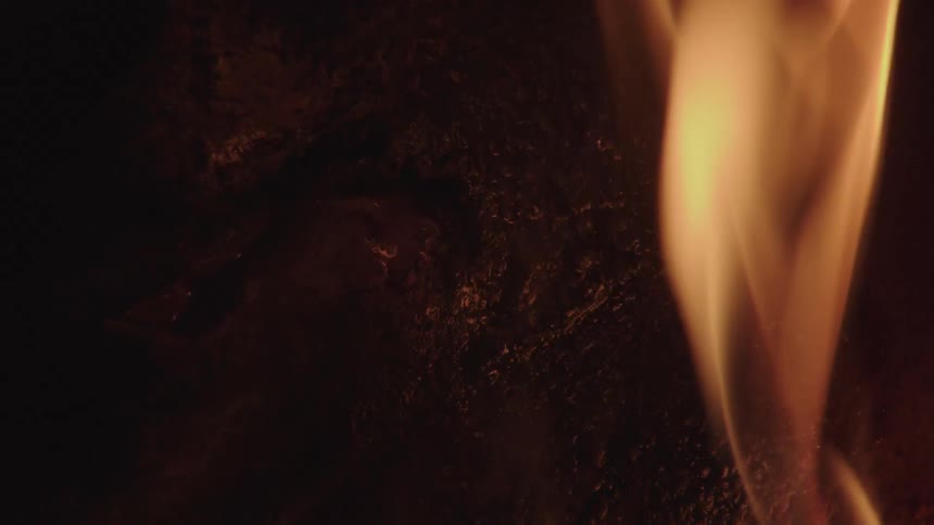 The flames of a bonfire moving randomly and with a bright orange light reflecting on a stone that is nearby