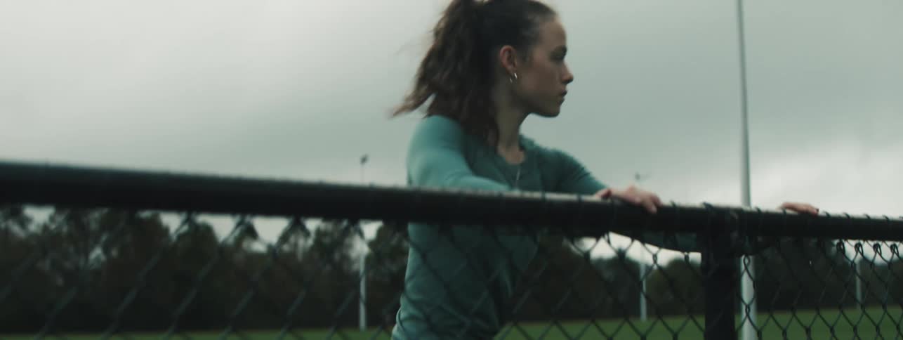Teenager warms up and stretches while holding onto a fence near a running track
