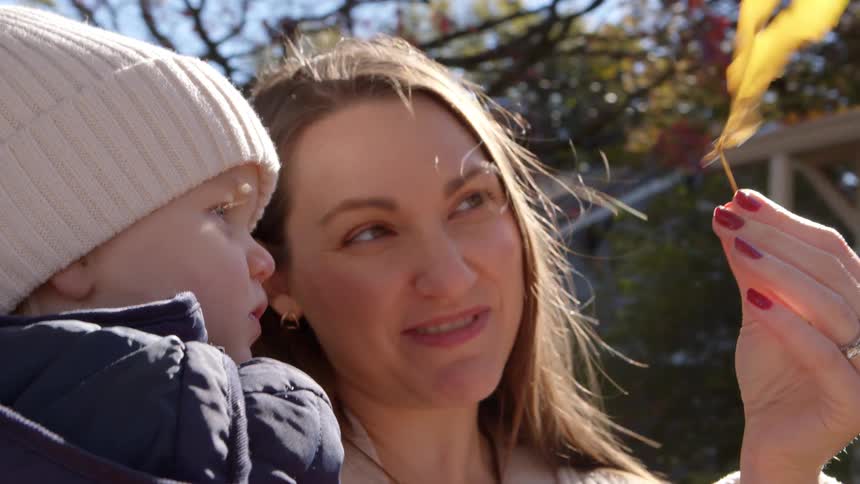 Woman with her son drinking on her lap showing an autumn leaf