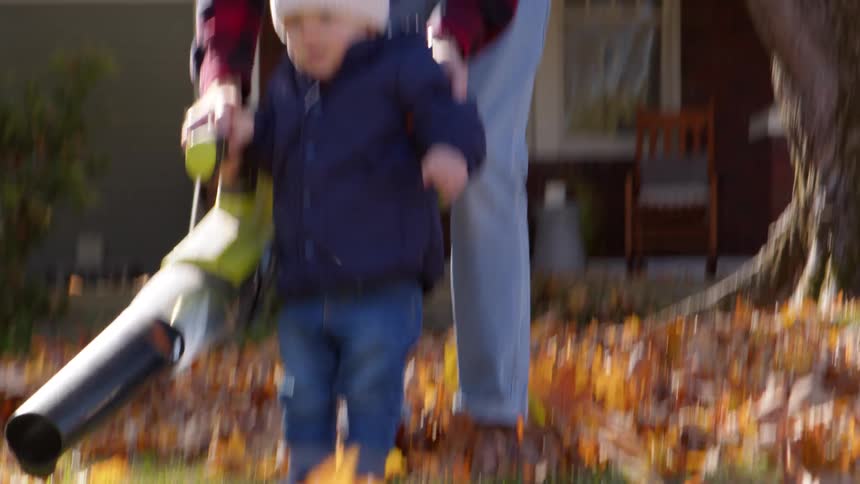 A father and son use a leaf blower to the leaves