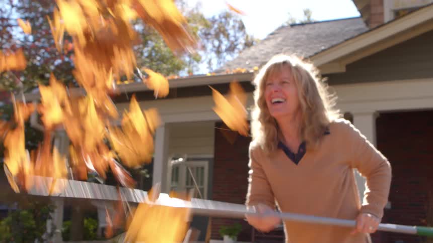 Woman having fun playing with dry leaves in a front yard