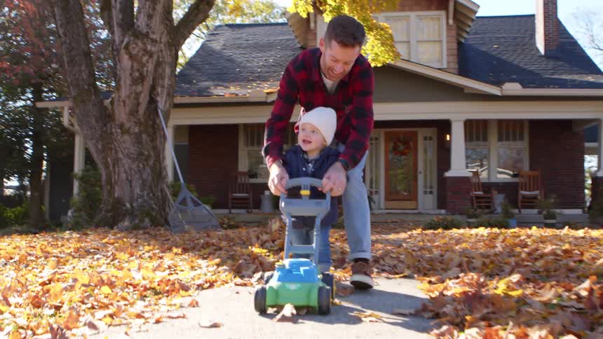 A boy is playing with a toy lawnmower in the yard