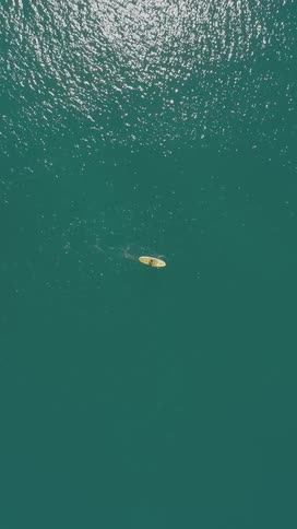 A birdseye view of a yellow boat cruising across the ocean at midday