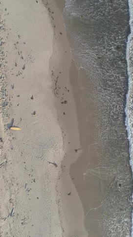 An aerial view of the beach as sea waves crash against the shore at midday