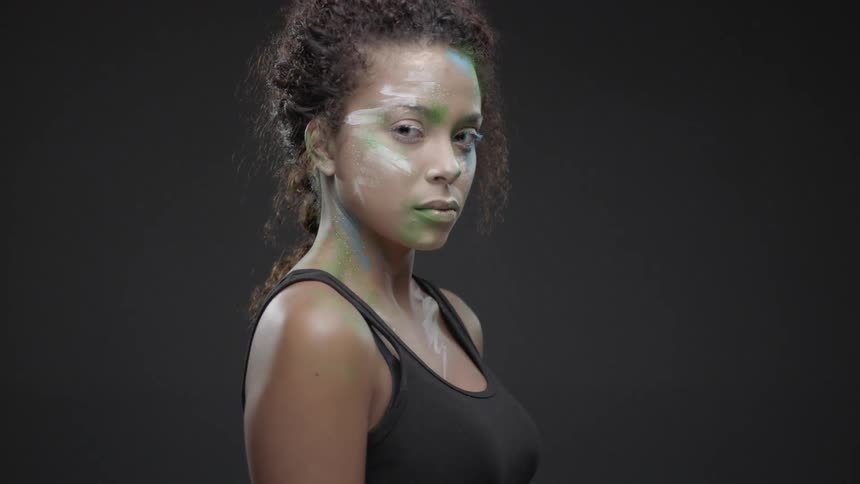 A woman with paint on her face turns to look forward