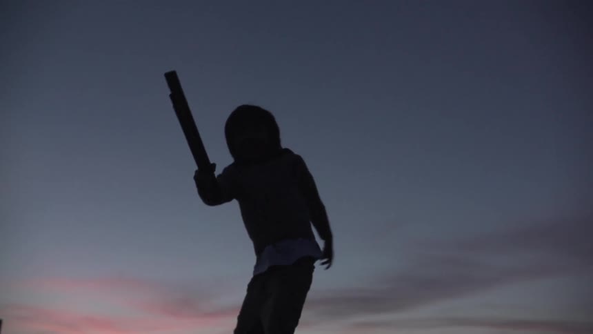 Child waving a stick around at sunset