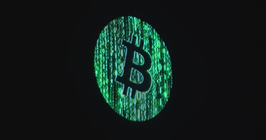 A digital screen displays a green bitcoin sign or logo animation consisting of the binary coding digits one or 1 and zero or 0 in a neon green color