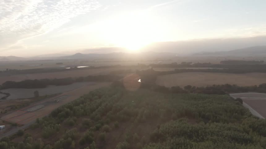 Sunlight breaks over a patchwork of farmland trees and winding roads with distant mountains on the horizon