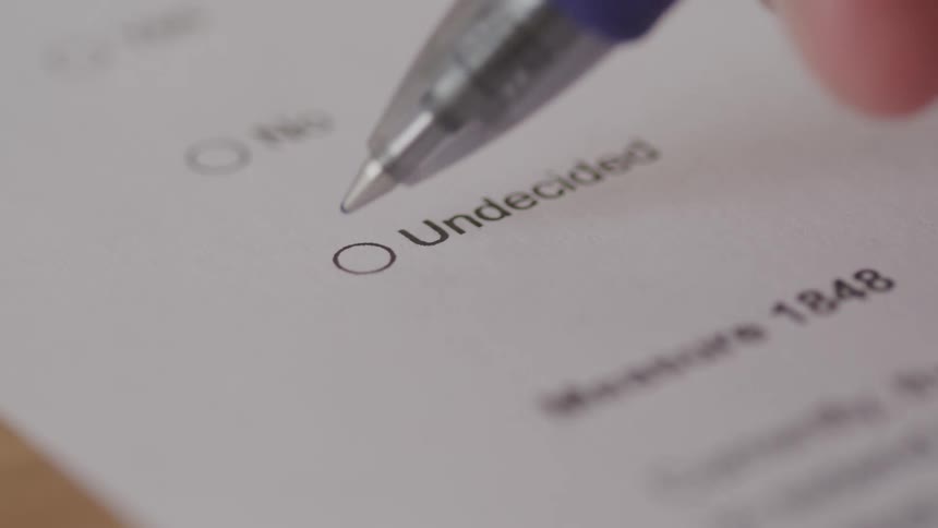 A hand holds a blue pen marking a circle around undecided on a white paper document