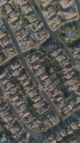 An overhead aerial view reveals a sprawling suburban residential neighborhood with numerous houses curving streets and green spaces