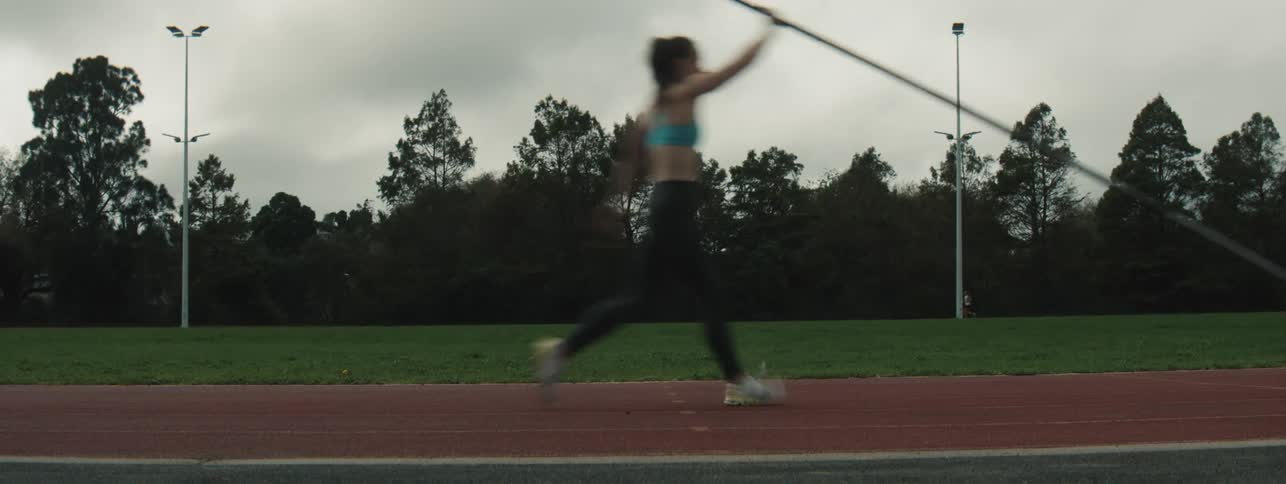 Female athlete runs on a track and attempts to plant a pole while practising for pole vault during daytime