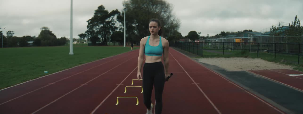 Female athlete walks back on a track while carrying a pole as she practises outdoors during daytime