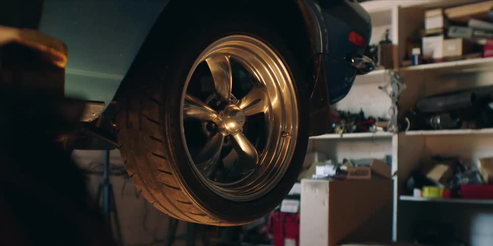 Close up of a tire attached to a car suspended in the air inside a motor workshop