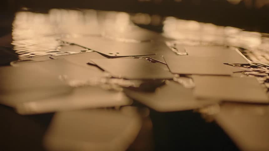 Cards drop and float on the surface as flames reflect on the water