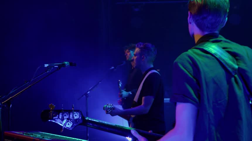 A band performing at night on stage with 3 people 2 playing guitar and 1 playing bass