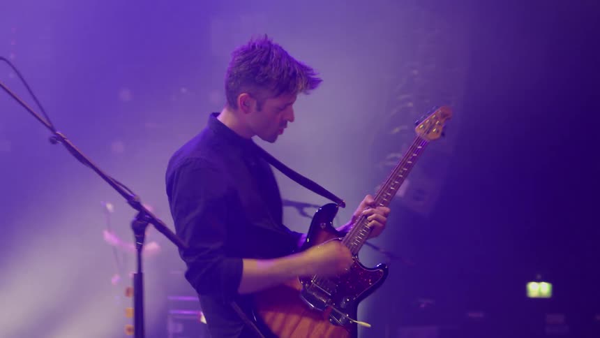 A guitarist playing his guitar on stage with his band