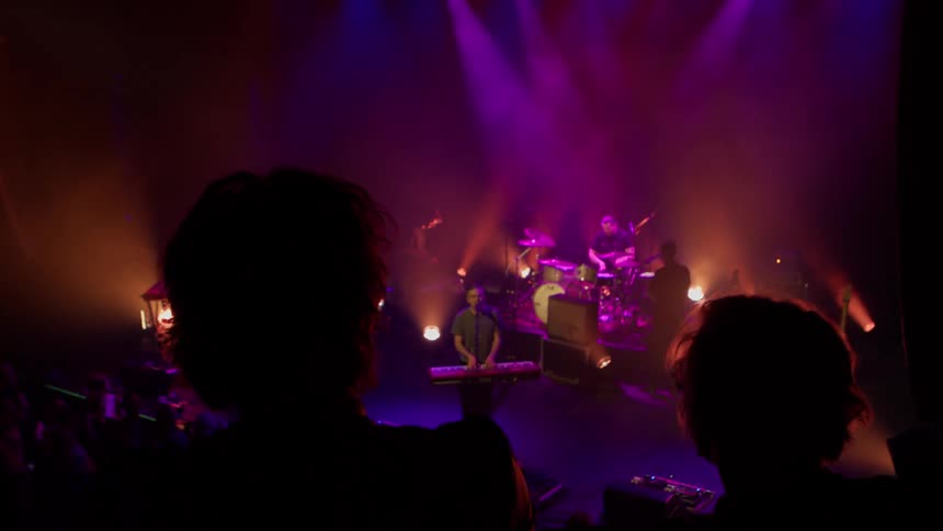A live concert featuring multiple artists including a guitarist drummer and keyboardist all performing together on stage