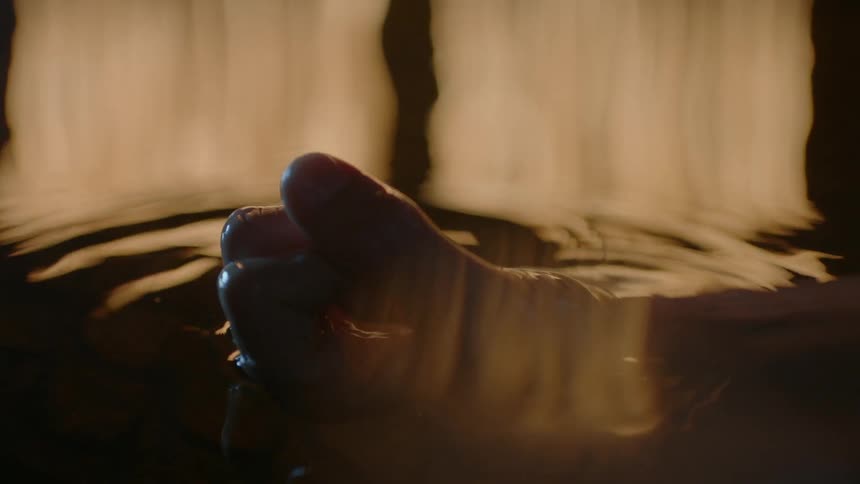 A hand is lifted out of water that is reflecting flames