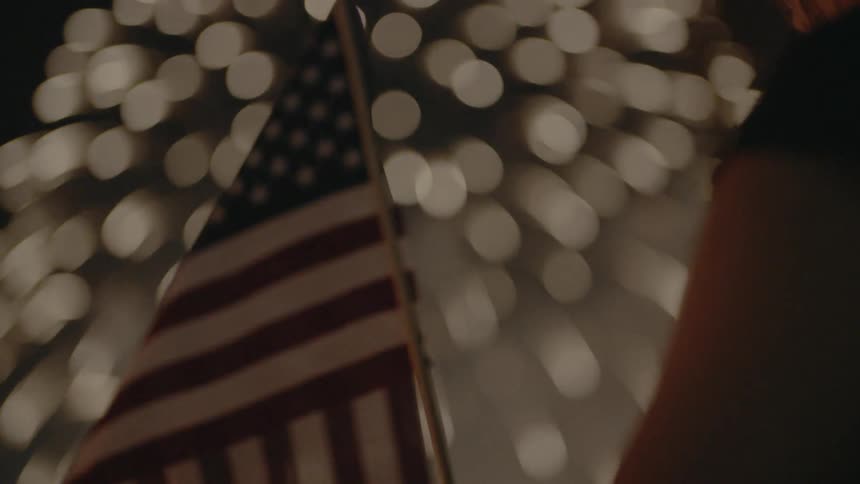 An american flag waves as fireworks explode overhead