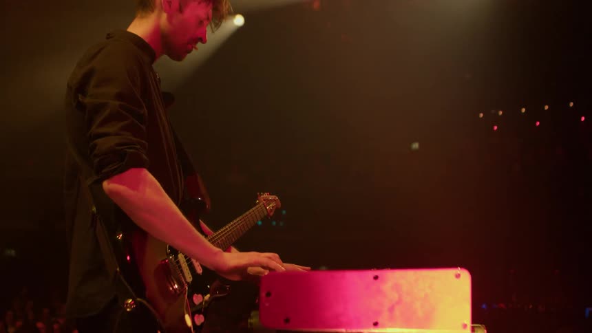 An artist playing the guitar on stage during a live concert performance as the crowd watches attentively