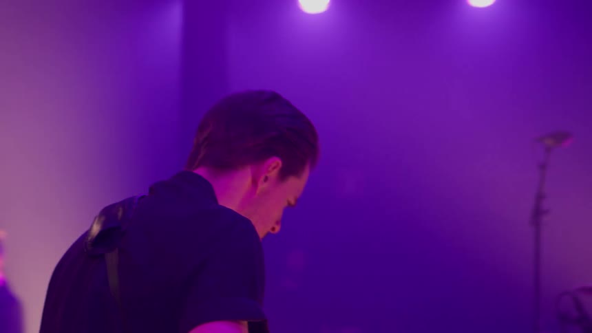 Three musicians perform onstage under purple lighting