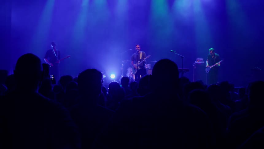 A group of musical artists performing live on stage during a concert playing guitars drums and singing to the crowd