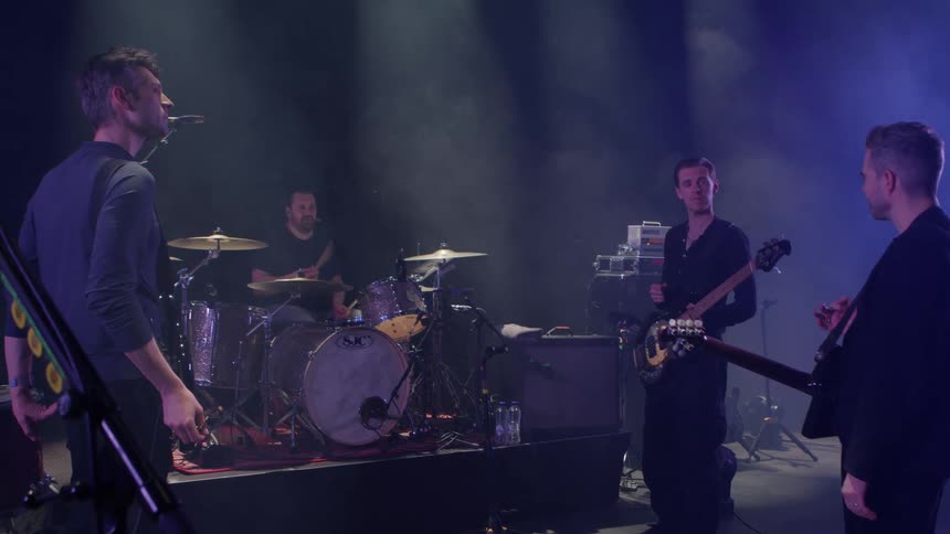 Band made up of four men talking to their respective musical instruments