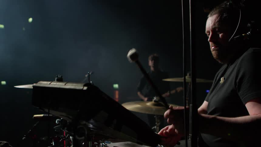 A man performs with a band in a concert while wearing a microphone headset