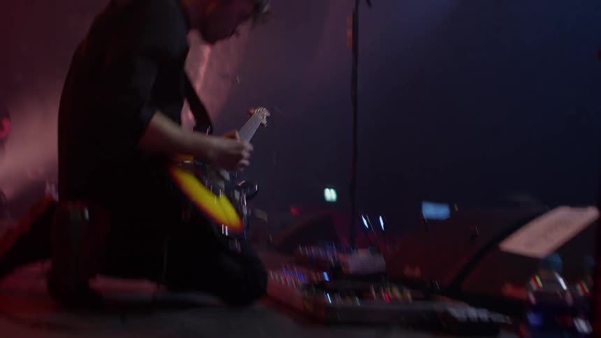 Guitarist plays and adjusts his soundboard with other musicians behind him
